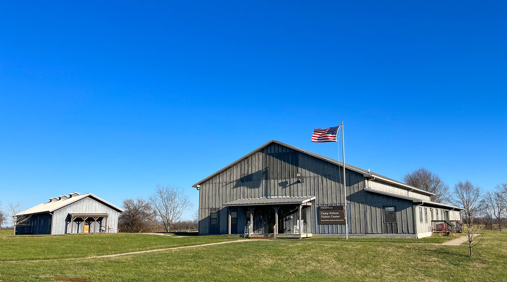 Gray-colored visitor center building with a U.S. flag in front on a large grass field