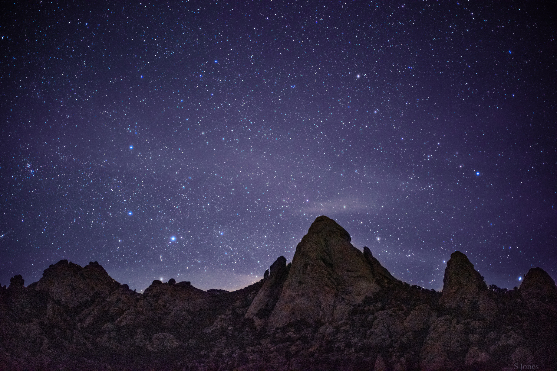 Stars glitter in the sky above granite formations on a mountainous ridgeline. 