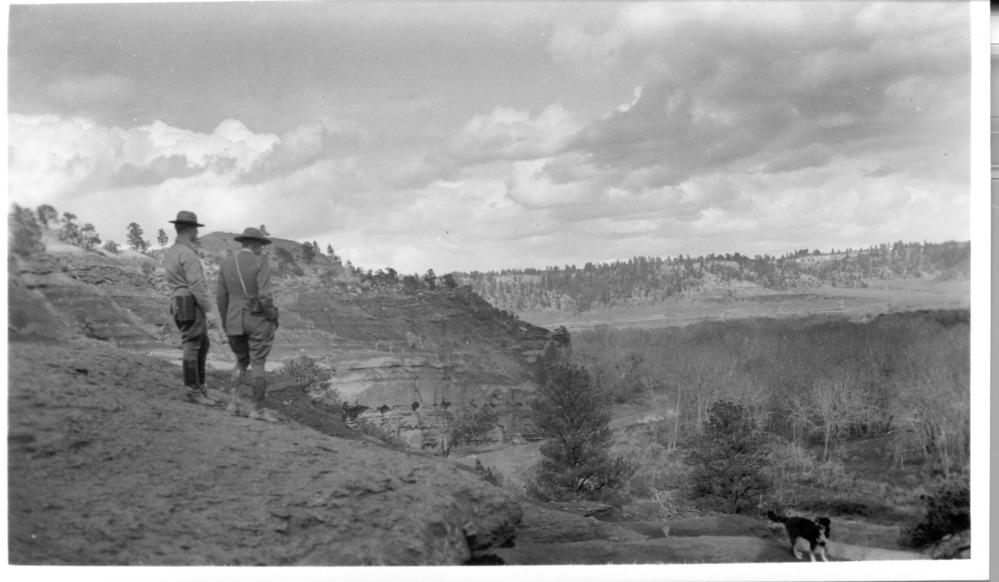 Two men stand on a bluff and look into the river valley below.