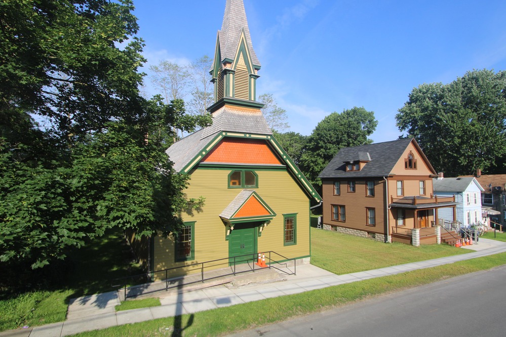 A green church building next to a brown house structure.