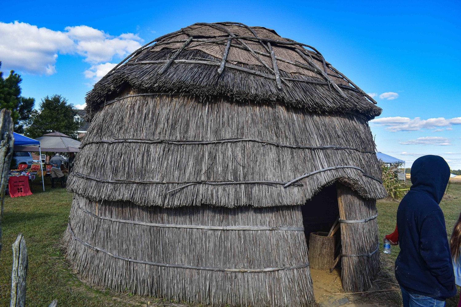 A Native American structure replica that is made of branches, sticks, and hemp with a dome roof can be seen in the middle of the image.