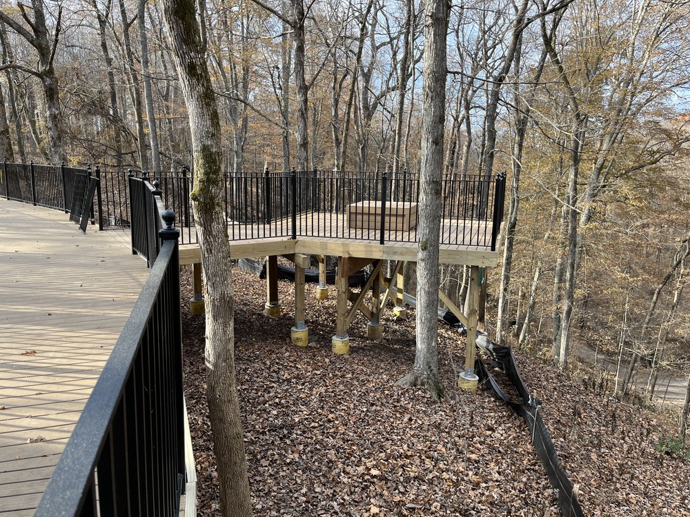 A wooden scenic overlook with black metal railings in a forest.