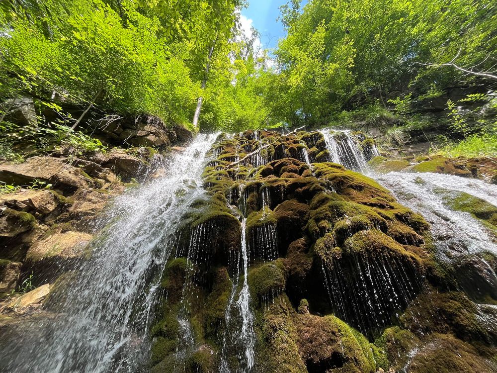 View looking up at a steep waterfall with moss-covered rocky walls