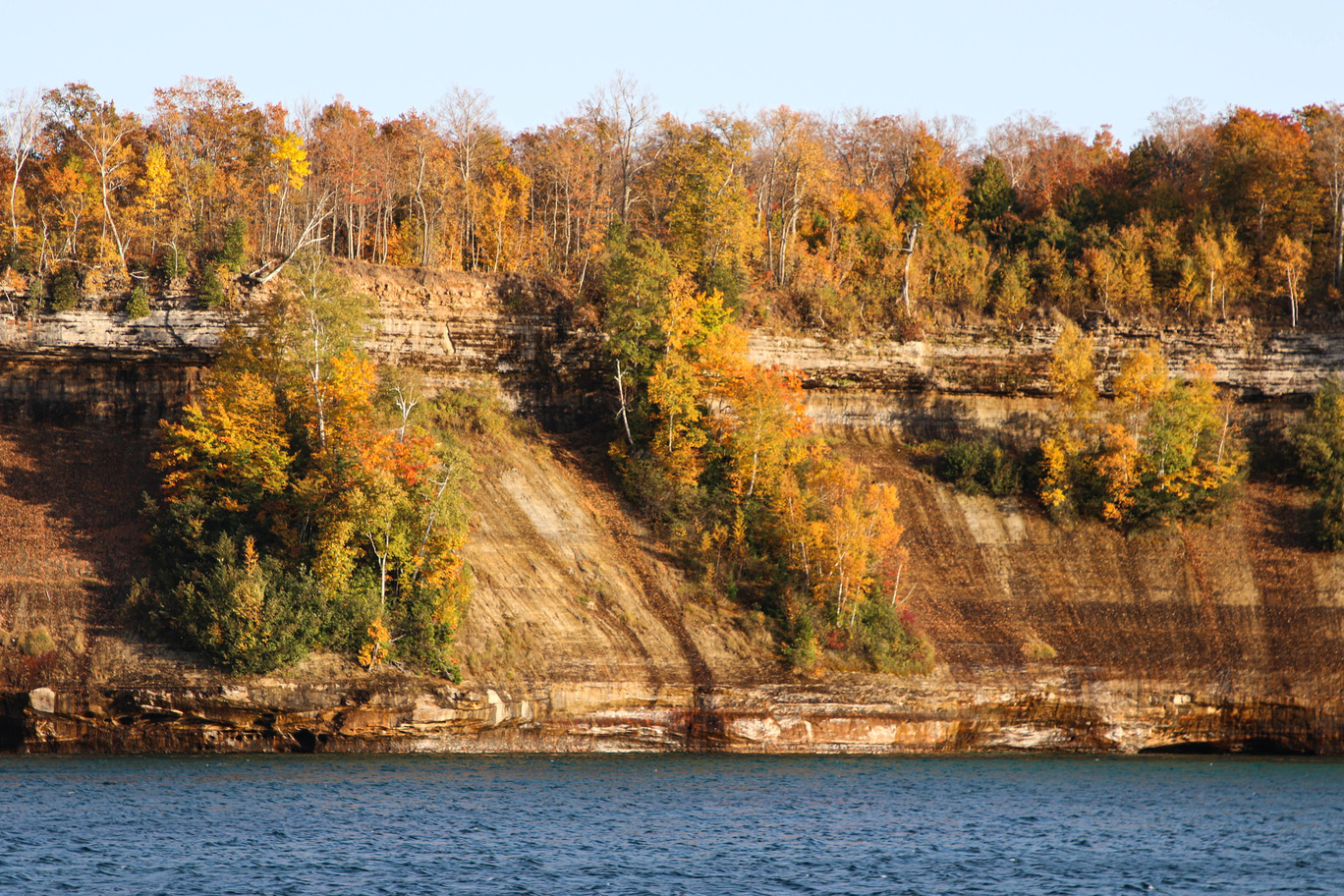 Tall forested cliffs covered in trees growing on top and the sides next to a large lake