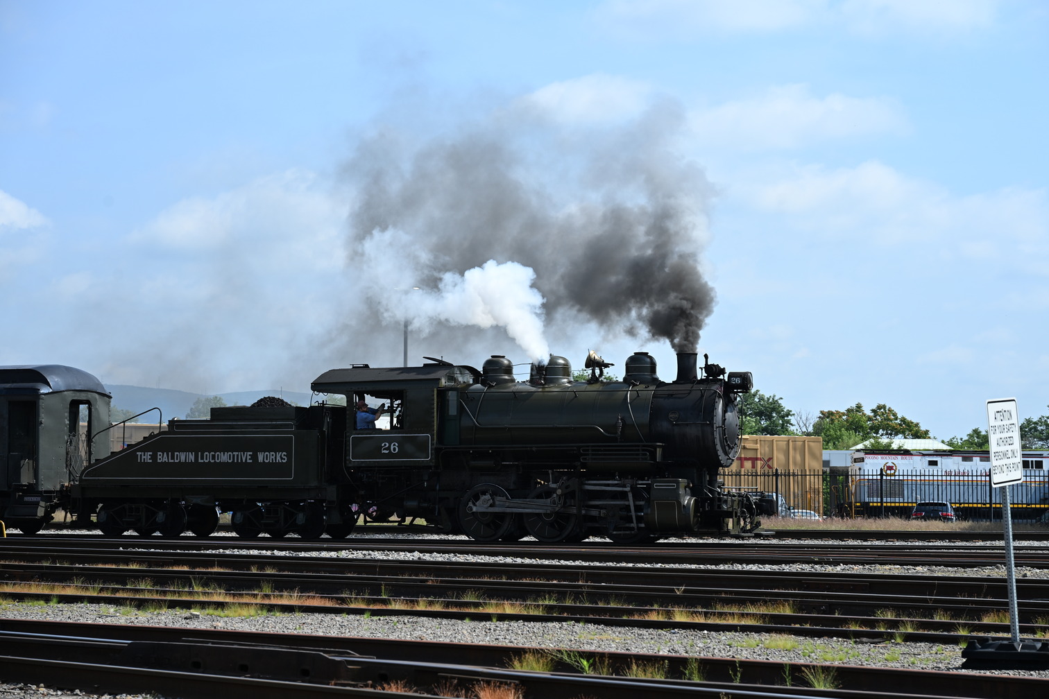 Steam Locomotive puffing white and dark gray smoke and moving along the tracks. 