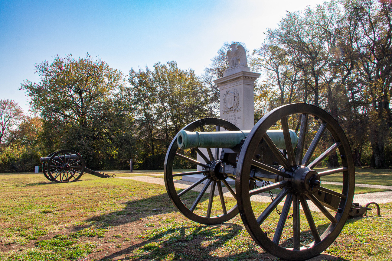 Two rusted cannons sit on opposite sides of a granite monument.